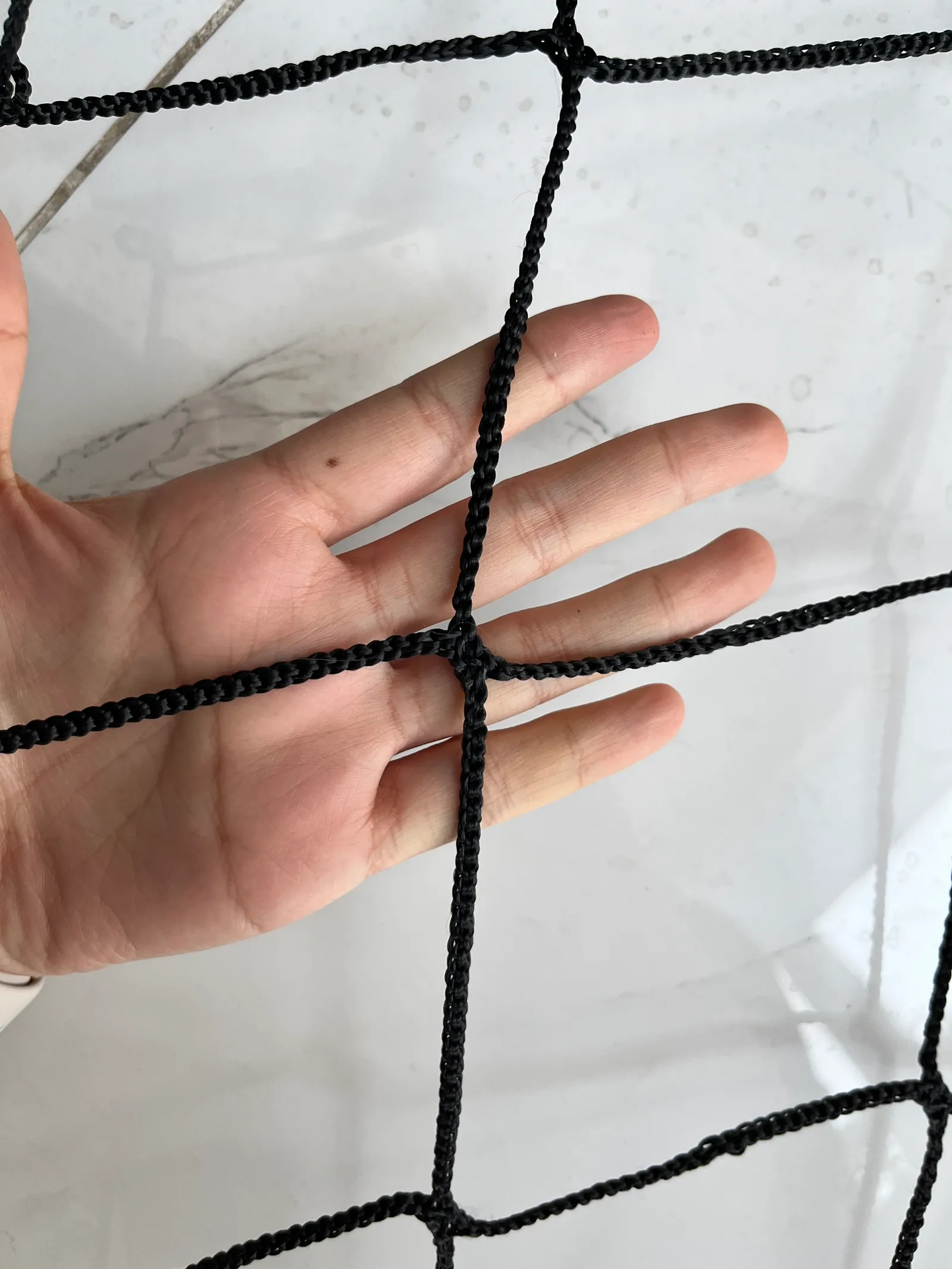 Black knotless polyester ball stop netting, 100 mm mesh, held in hand