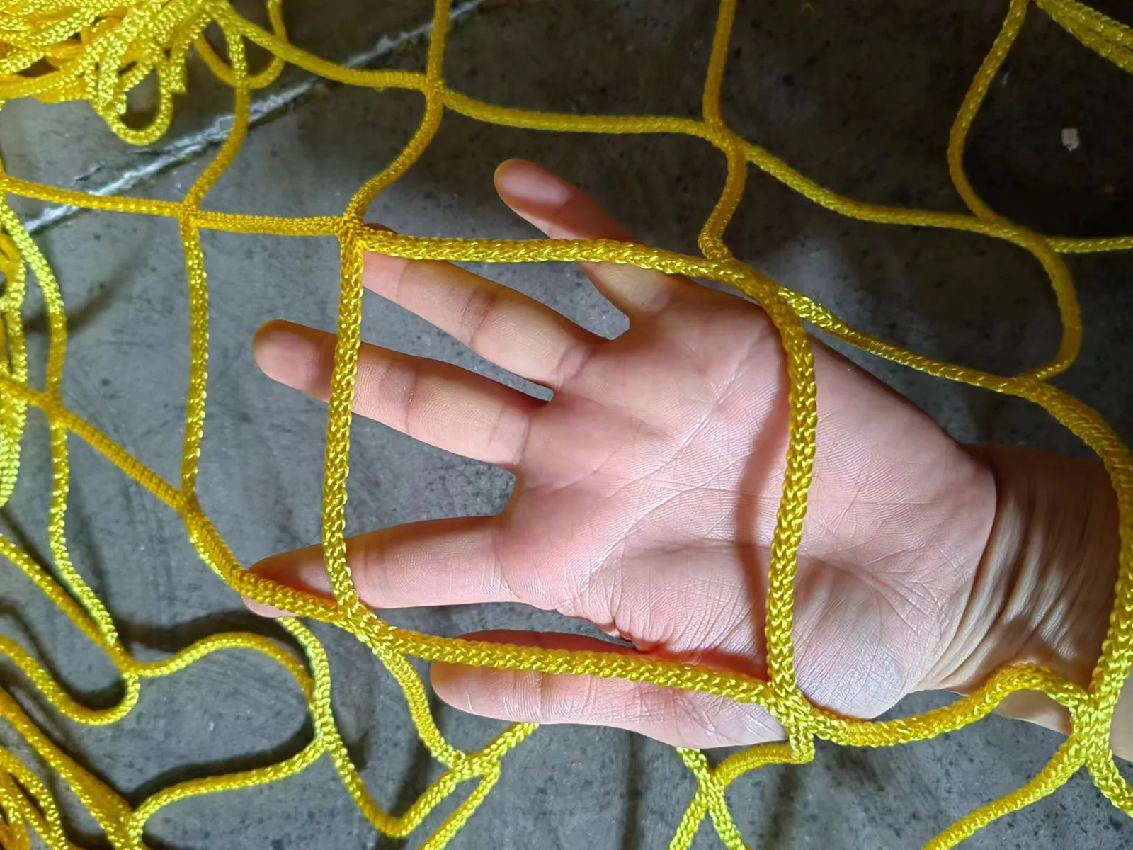 Yellow knotless polyester ball stop netting, 100 mm mesh, 5 mm twine, held in hand