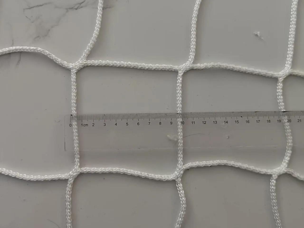 Knotless netting measured against a rule in the photograph: one mesh opening spans 100 mm
