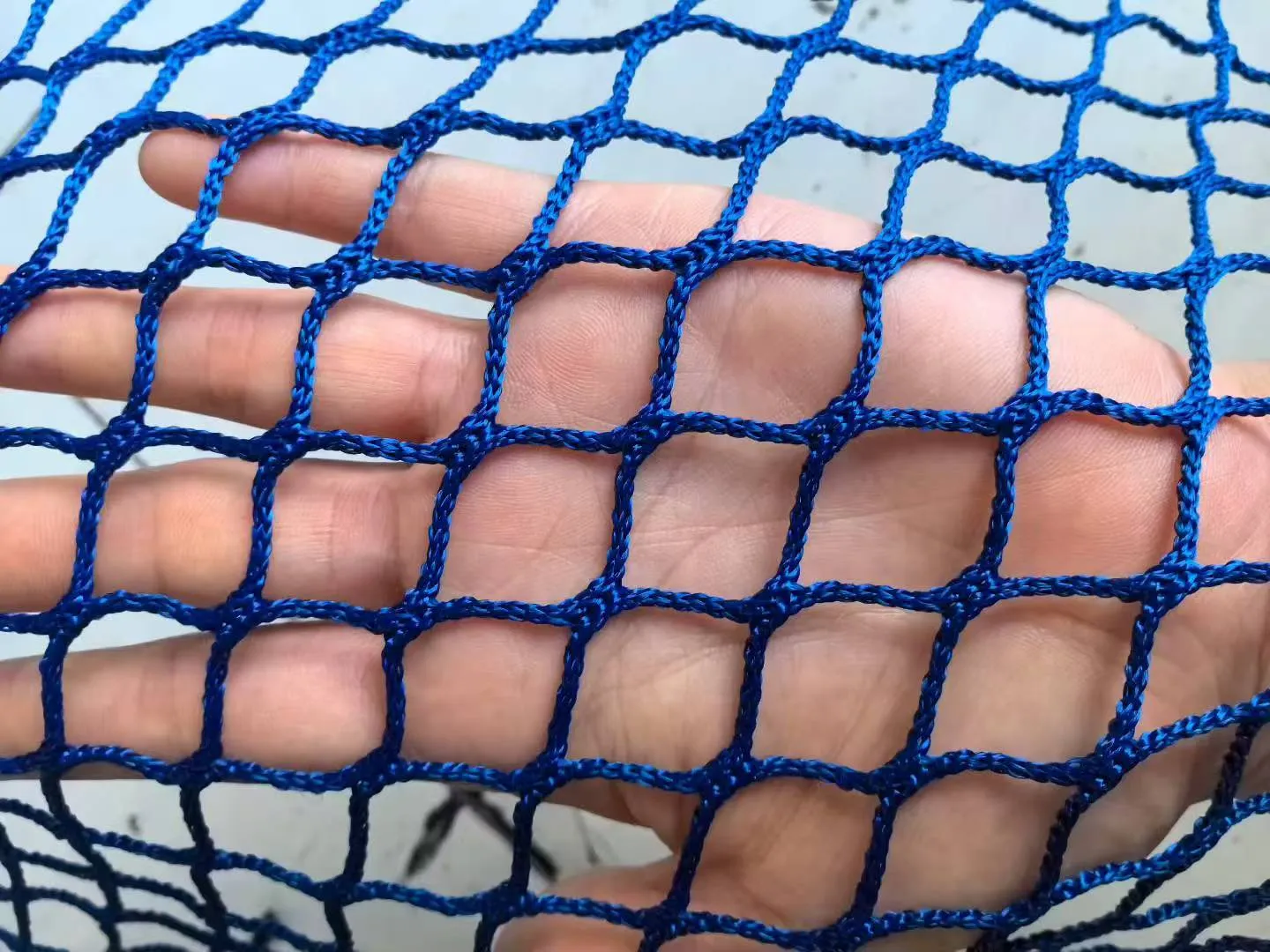 Blue golf barrier netting, 20 mm mesh, 2 mm twine, factory sample held in hand