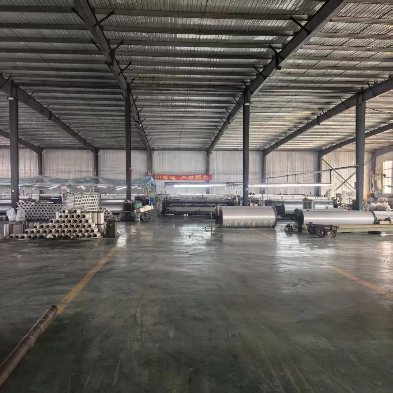 Vista amplia de la nave de producción en las instalaciones del socio fabricante, telares y rollos de material bajo una estructura metálica